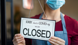 Title image for How Employee Retention Tax Credits Can Help You Recover from COVID-19 showing a woman putting up a sign at the front of a store that reads "sorry due to Covid-19 we are closed".