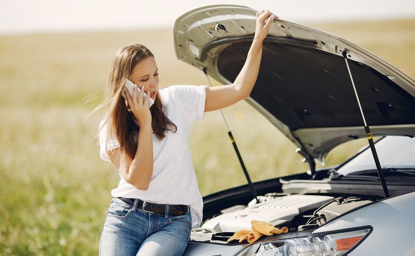 Title image for UM and UIM Coverage, Exclusions, and Endorsements showing a woman stranded in the middle of the road sitting on the hood of her car calling her insurance carrier.